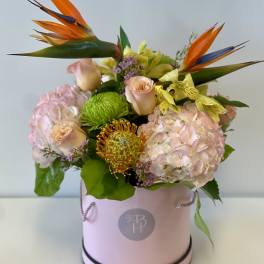 Pink floral arrangement in a round box with orange bird-of-paradise blooms