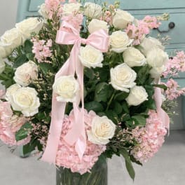 White roses and pink hydrangeas in a glass vase with a pink ribbon