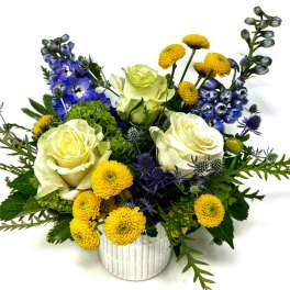 White roses, yellow pom flowers, and blue blooms in a white vase
