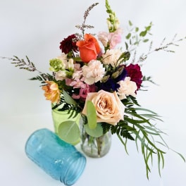 Mixed bouquet of roses, carnations, and snapdragons in a glass vase