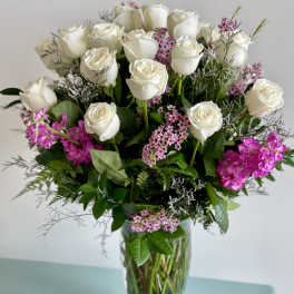 White roses and pink filler flowers arranged in a clear glass vase