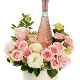 Bottle of pink sparkling wine surrounded by pink roses and white flowers in a white round container