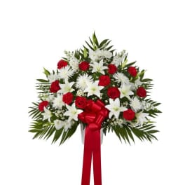 Fan-shaped standing arrangement of red roses and carnations with white lilies and mums, finished with a red bow and ribbon