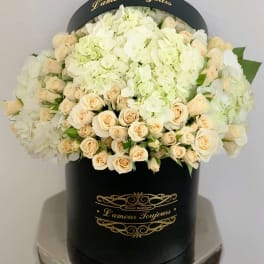 Round black hatbox filled with cream roses and white hydrangeas with gold L'amour Toujours lettering