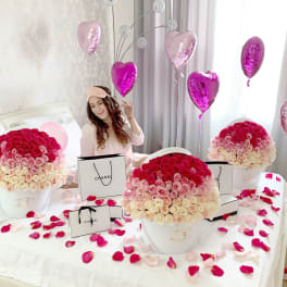 Large hatbox arrangements of pink and white roses on a bed with heart balloons and gift bags.
