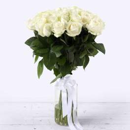 Tall arrangement of white roses in a clear glass vase with a white ribbon bow.