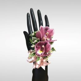 Wrist corsage of pink orchids and small white flowers on a black mannequin hand