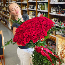 Woman holding a large bouquet of red roses with a pink ribbon