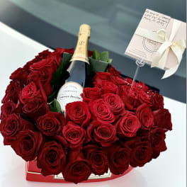 Red rose arrangement surrounding a champagne bottle in a gift box