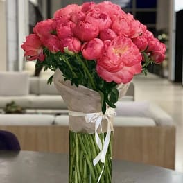Bouquet of bright pink peonies in a tall glass vase with a ribbon wrap