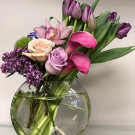 Bouquet of purple tulips, pink calla lilies, roses, and orchids in a glass vase