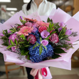 Bouquet of pink and purple flowers with blue hydrangeas wrapped in pink paper