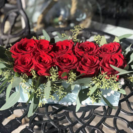 Red roses arranged in a low rectangular box with greenery