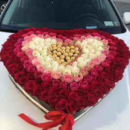 Heart-shaped rose arrangement with chocolates and a red ribbon