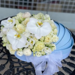 White rose and orchid bouquet in a light blue hatbox with a sheer ribbon