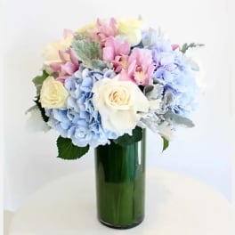 Pastel bouquet of hydrangeas and roses in a green glass vase