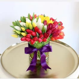Colorful tulip bouquet in a glass vase with a purple ribbon