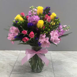 Bouquet of pink, yellow, and purple flowers in a glass vase with a pink ribbon