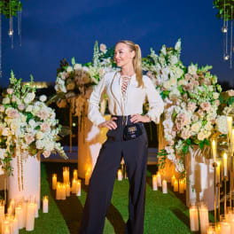 Woman posing between large floral arrangements and candles at night