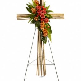 Tall bamboo cross on a metal easel accented with orange roses and clustered blooms.