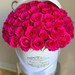 Hot pink roses densely arranged in a white hatbox-style container with gold script text