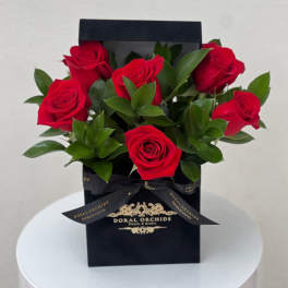 Arrangement of red roses in a black gift box with gold logo and bow