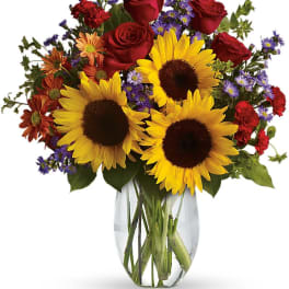 Bouquet of sunflowers, red roses, and purple daisies in a glass vase