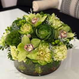 Green floral arrangement in a low glass bowl with orchids and hydrangeas
