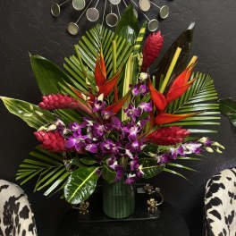 Tropical arrangement with purple orchids and red heliconia in a green vase