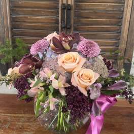 Mixed bouquet of peach roses, orchids, and purple blooms in a glass vase