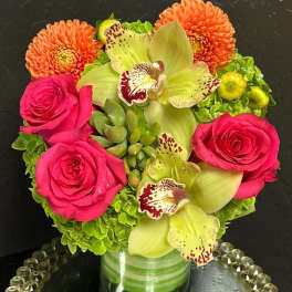 Pink roses and green orchids arranged with orange dahlias in a glass vase.