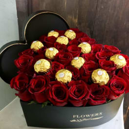 Red roses and gold-wrapped chocolates in a black heart-shaped box
