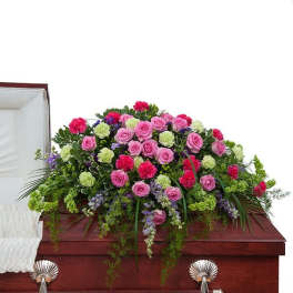 Pink and green floral casket spray with roses and carnations on a wooden casket