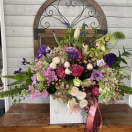 Large mixed floral arrangement in a white vase with pink ribbon