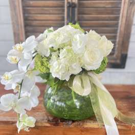 White orchid and rose arrangement in a green glass vase with ribbon