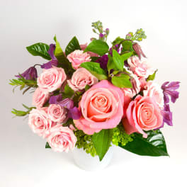 Pink roses and purple flowers arranged in a white vase