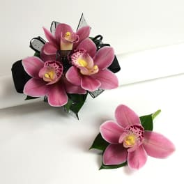 Pink cymbidium orchid wrist corsage with black ribbon and matching boutonniere on white surface
