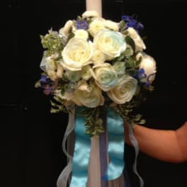 White rose floral arrangement with a tall candle and blue ribbons