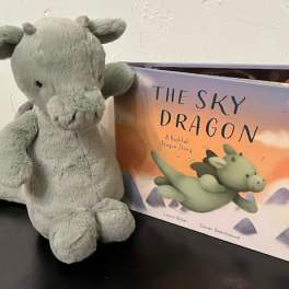 Gray plush dragon beside a children's book titled The Sky Dragon