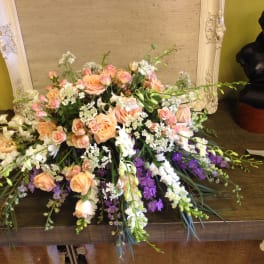 Low floral arrangement with peach roses, white blooms, and purple flowers