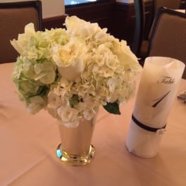 White floral centerpiece in a tall vase beside a rolled napkin