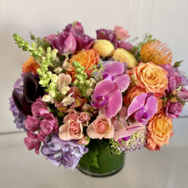 Mixed bouquet of pink, orange, purple, and yellow flowers in a glass vase
