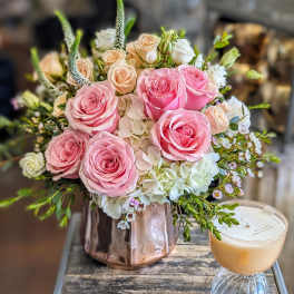 Pink and peach roses arranged in a metallic vase with a candle beside it