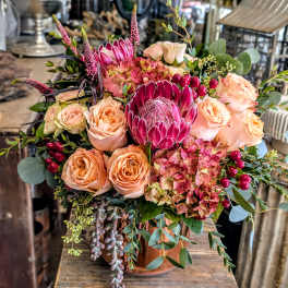 Peach roses and pink protea in a copper vase