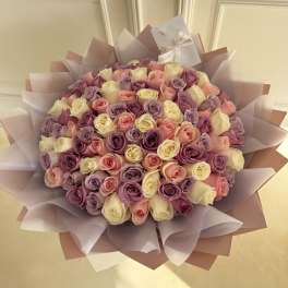 Large bouquet of pink, lavender, and cream roses wrapped in pastel paper