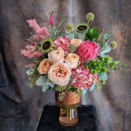 Bouquet of peach roses, pink hydrangea, and a pink protea in a glass vase