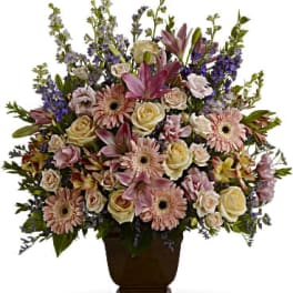 Tall arrangement of pink lilies, gerbera daisies, and cream roses in a brown urn-style vase
