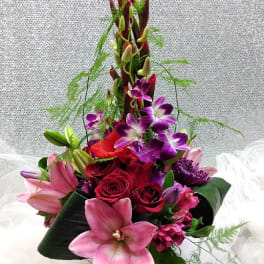 Tall bouquet of pink lilies, red roses, and purple orchids in a glass vase