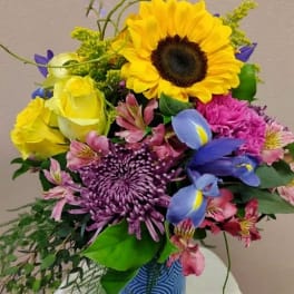 Colorful bouquet with sunflower, roses, and purple blooms in a blue vase