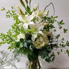 White lilies and hydrangea in a glass vase with airy greenery
